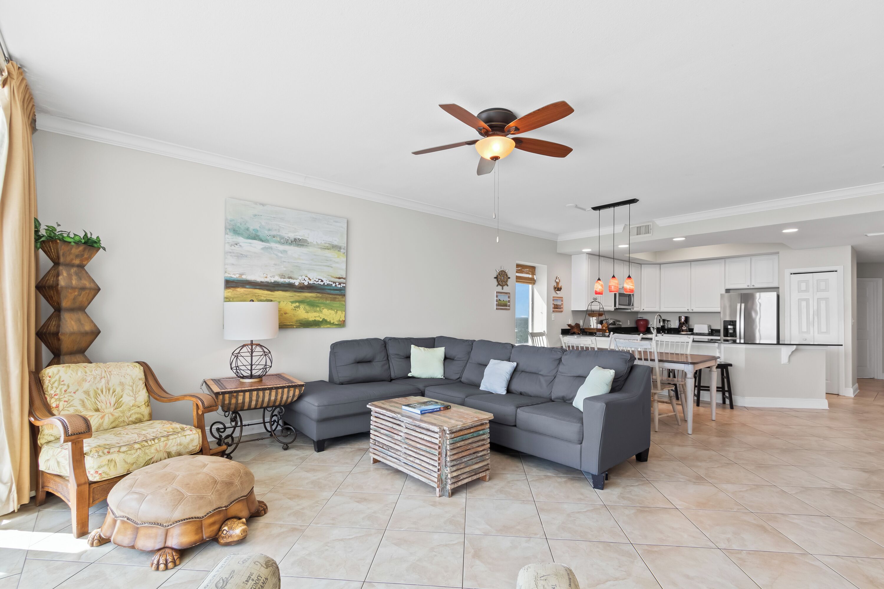 A living room with a sectional sofa, a coffee table, a turtle-shaped ottoman, a wooden side table, a floor lamp, and a ceiling fan.