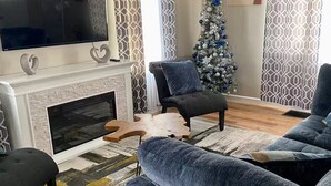 Ein Wohnzimmer mit Kamin, Fernseher und einer Weihnachtstanne, ausgestattet mit blauen Sofas.