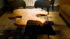 Ein Wohnzimmer mit einem einzigartigen Holztisch, zwei Sesseln mit gemusterten Kissen, einem kleinen Beistelltisch und einer Couch.