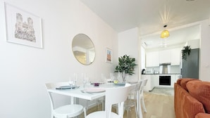 A dining area with a white table set for four, a round mirror, and a framed picture on the wall. - Le Central: 6 travelers in the city center with Wi-Fi (Reims)