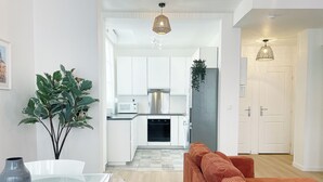 A modern kitchen with white cabinets, a stainless steel refrigerator, and a microwave. There is a dining table with a vase and a plant. - Le Central: 6 travelers in the city center with Wi-Fi (Reims)