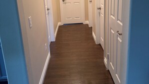 A hallway with a wooden floor, white doors, and light-colored walls. - Charming 2-bedroom Rosena Casita with private 1-car garage and private entrance. (San Bernardino)