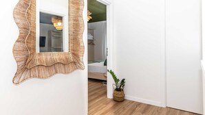 Un pasillo con un espejo tejido, una planta en maceta y una cama con una manta verde.