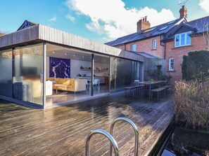 A modern house with a glass-enclosed living area, a wooden deck, and a brick exterior. - Bredy Cottages (Bridport)