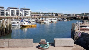 A marina with boats docked, a wooden walkway, and buildings in the background. - Bredy Cottages (Bridport)