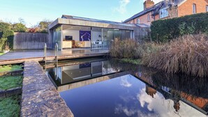A modern house with a glass-enclosed living area, a pool, and a wooden deck. - Bredy Cottages (Bridport)