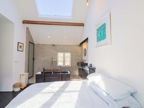 A bedroom with a skylight, a large bed, a bathroom with a bathtub, and a view of the outdoors. - Bredy Cottages (Bridport)