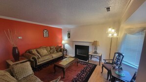 Una sala de estar con sofá, sillones, chimenea, candelabro y una mesa de comedor.