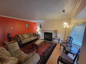 A living room with a sofa, armchairs, a fireplace, a chandelier, and a dining table. - Spacious 4-bedroom house in enchanting Greensboro near UNCG (Greensboro)