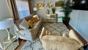 A living room with a sofa, armchairs, a side table, a lamp, a console table with decorative items, and a large plant.