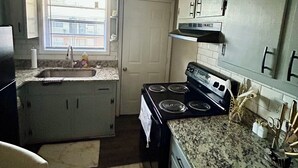 A compact kitchen with a sink, stove, and granite countertop.