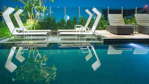 An indoor swimming pool with multiple lounge chairs and a sunbed, surrounded by greenery and a glass barrier. - Hoc5 Daily Apartment Chiang Mai (Chiang Mai)