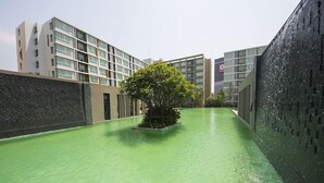 A modern building with a green pool area, surrounded by high-rise structures. - D Condo Sign Chiang Mai R628 (Chiang Mai)