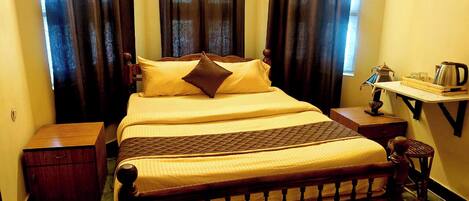 Una cama con estructura de madera, una mesita de noche con una lámpara, y una pequeña mesa con una tetera y una taza.