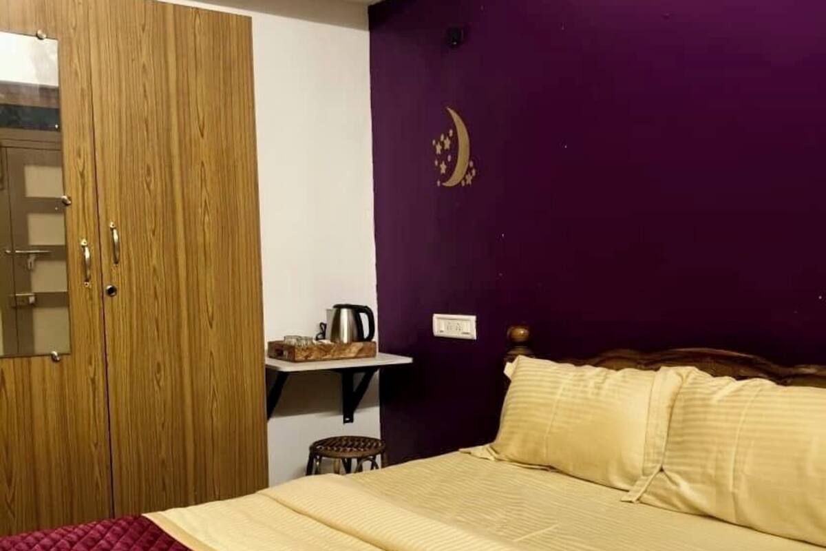 A bedroom with a bed, wooden wardrobe, and a purple wall with a crescent moon design.