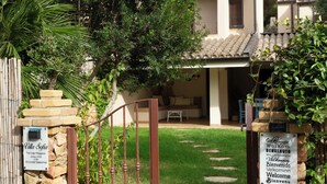 A villa with a stone gate, a sign welcoming visitors, and a pathway leading to the entrance. - Villasimius - Villa Sofia (Cala Caterina)