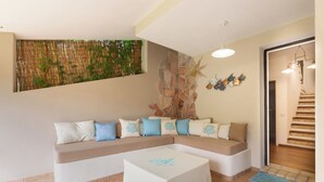 A living room with a beige sectional sofa, a white coffee table, and a decorative wall with a bamboo plant. - Villasimius - Villa Sofia (Cala Caterina)