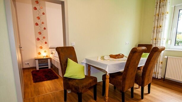 A dining area with a table and chairs, a red rug, a wall with a floral design, and a window with curtains.