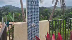 A tiled wall with a sign instructing to shower before entering the pool, surrounded by palm trees and a view of hills. - Piscina Vista Guest House w/ Solar & Pool (Ceiba)