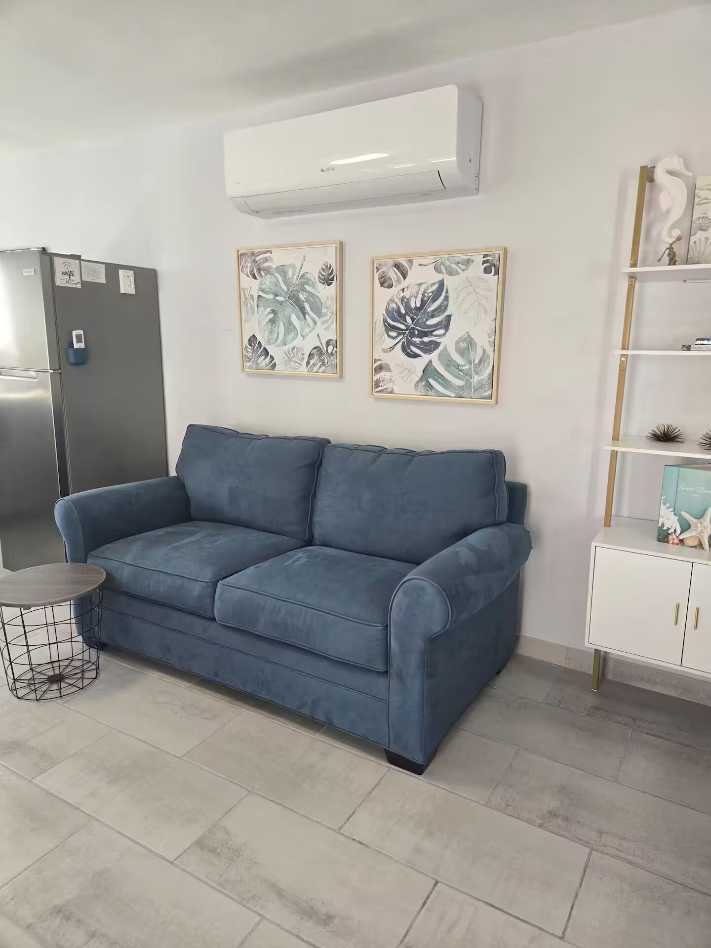 A modern living room with a blue sofa, a white cabinet, and two framed leaf artworks on the wall.