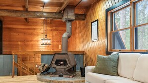 A cozy cabin interior with a wood-burning stove, a sofa, and a staircase. - The Log Haus - Minutes from Cuyuna, Miles from Ordinary (Crosby)