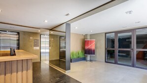 A modern lobby with a reception desk, elevators, and a large glass door leading to another area. - Complete Studios in Perdizes - CEP (São Paulo)