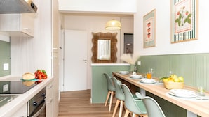 Eine moderne Küche mit Essbereich, mit einem Holztisch, grünen Stühlen und einer Kücheninsel mit integriertem Backofen.