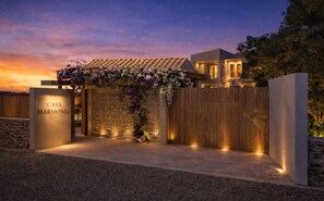 A modern villa with a stone facade, a wooden fence, and a pergola with flowers.