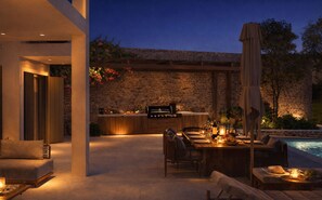 A modern outdoor dining area with a stone wall backdrop, a pool, and a barbecue grill.