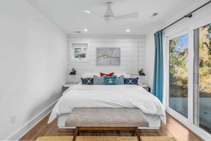 A bedroom with a bed, a bench, a ceiling fan, a window with curtains, and a wall-mounted artwork.