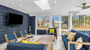 Uma sala de estar moderna com uma televisão de tela plana grande, móveis de madeira e grandes janelas com vista para o exterior.