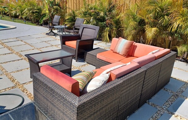 A patio area with a wicker sofa, a glass-top table, and chairs.