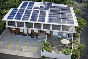A building with multiple solar panels on the roof, a parking area, and a small garden with plants. - Sustainable Stay Near Culebra | Free Parking | Solar Panels (Ceiba)