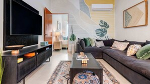 Een moderne woonkamer met een flatscreen televisie, een leren bank in donkere tint, een getextureerd vloerkleed en een minimalistisch ontwerp aan de muur.