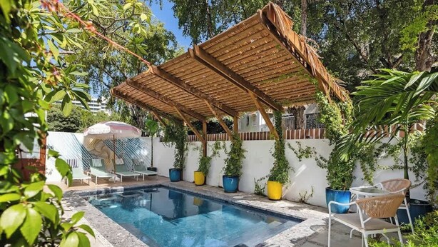 Zwembad met een houten pergola, ligbedden en plantenpotten.