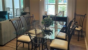 A dining area with a glass table, chairs, and a hanging light fixture. - Feels like Home on Hilton Head Island (Hilton Head Island)