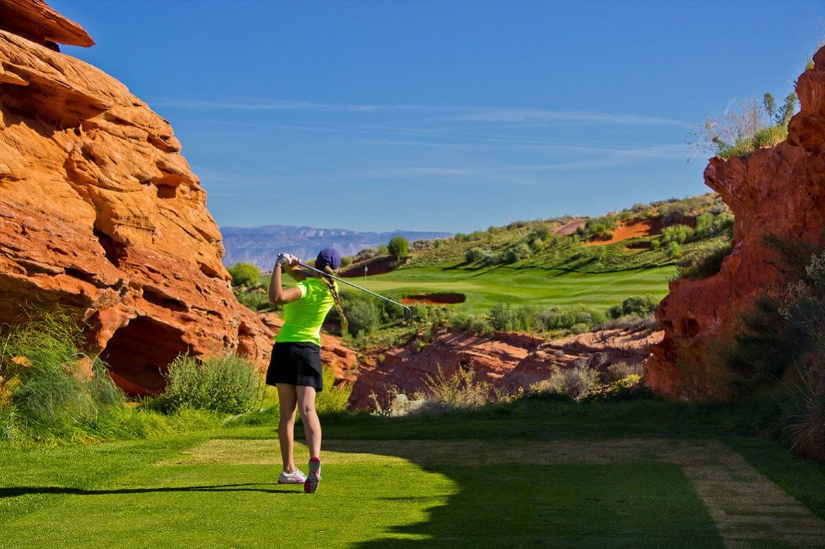 Un parcours de golf avec une formation rocheuse à gauche et un ciel bleu dégagé.