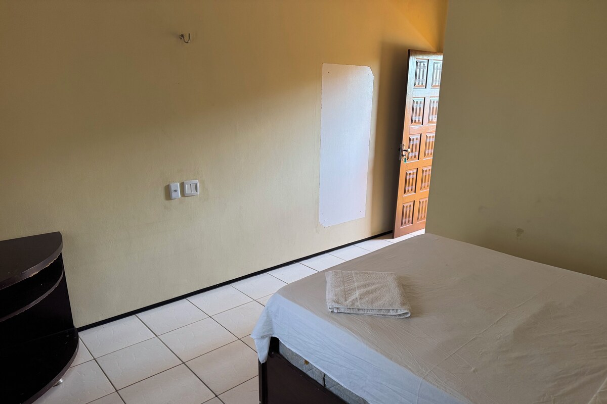 Une chambre d’hôtel avec un lit, une petite table, un interrupteur fixé au mur et une porte donnant sur une autre pièce.