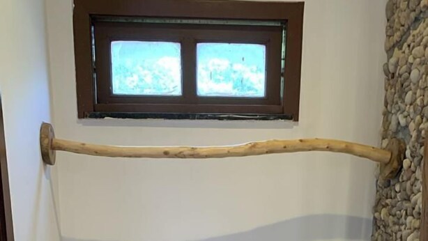 Une salle de bain avec une étagère en bois où sont pliés des serviettes, une petite fenêtre au-dessus et un mur en pierre.
