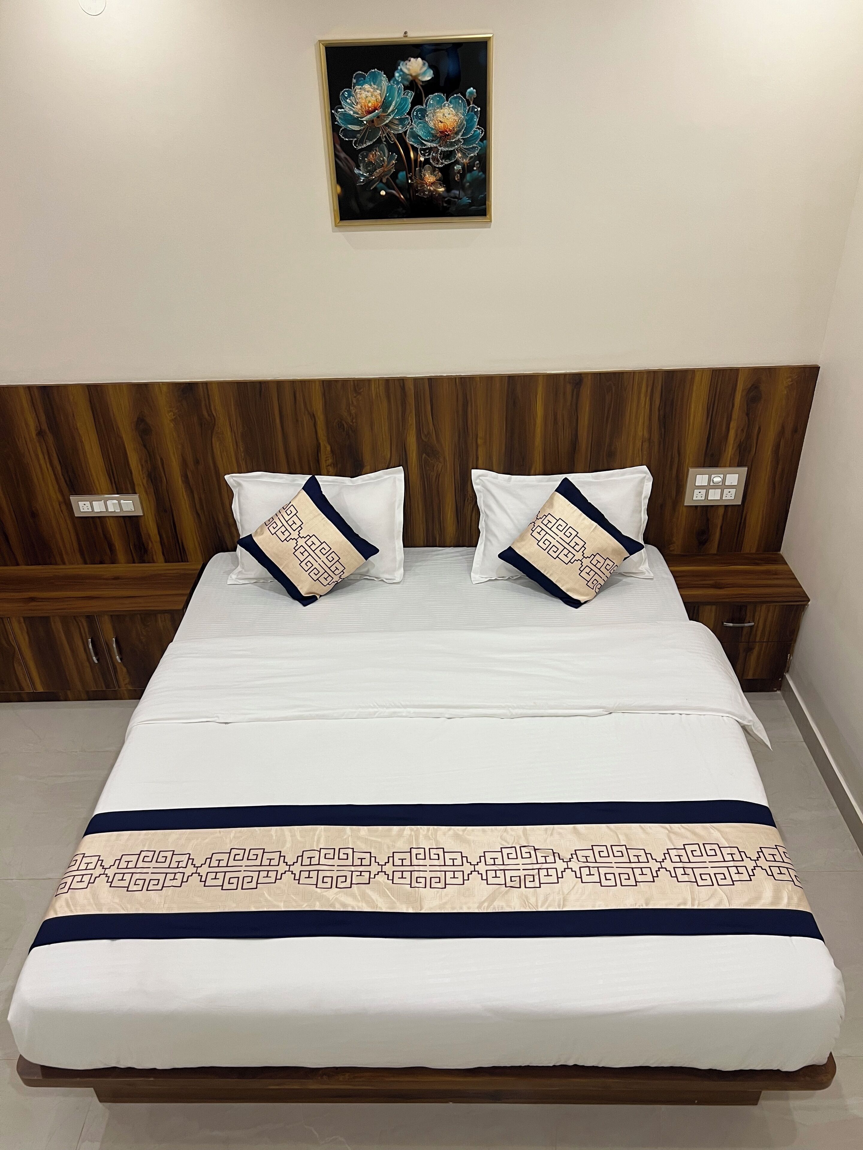 A neatly made bed with a patterned bedspread and two decorative pillows, a wooden headboard, and a framed artwork above the bed.