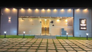Un edificio moderno con una entrada bien iluminada, un logotipo visible y un área pavimentada con césped al frente.
