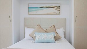 Ein Schlafzimmer mit einem Bett, einem Kopfteil und einem gerahmten Bild von einer Strandansicht.