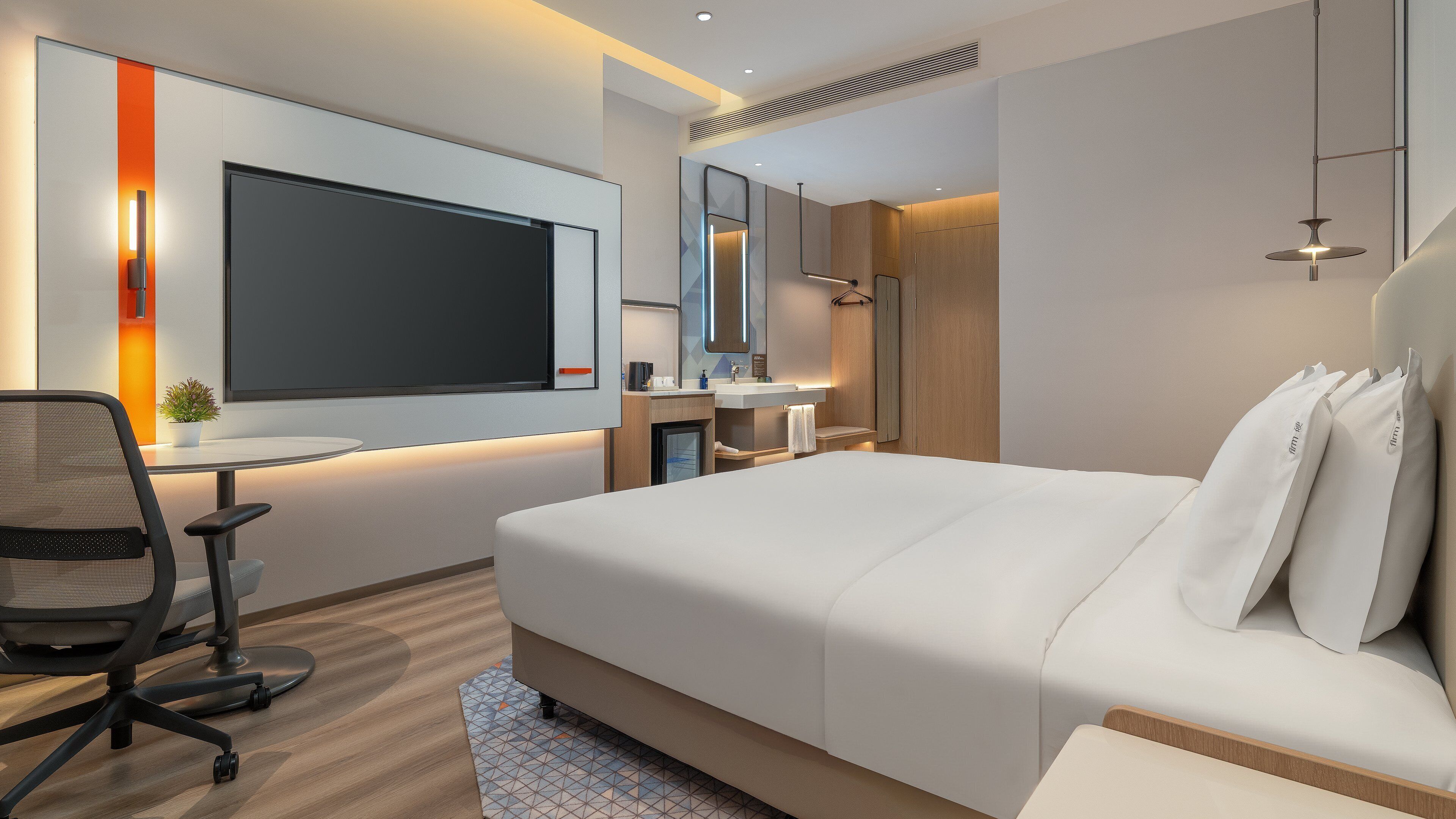 Une chambre d’hôtel moderne équipée d’un grand lit, d’un bureau avec un ordinateur, d’une chaise, d’une petite table, d’un miroir et d’une salle de bain avec un lavabo et un porte-serviettes.