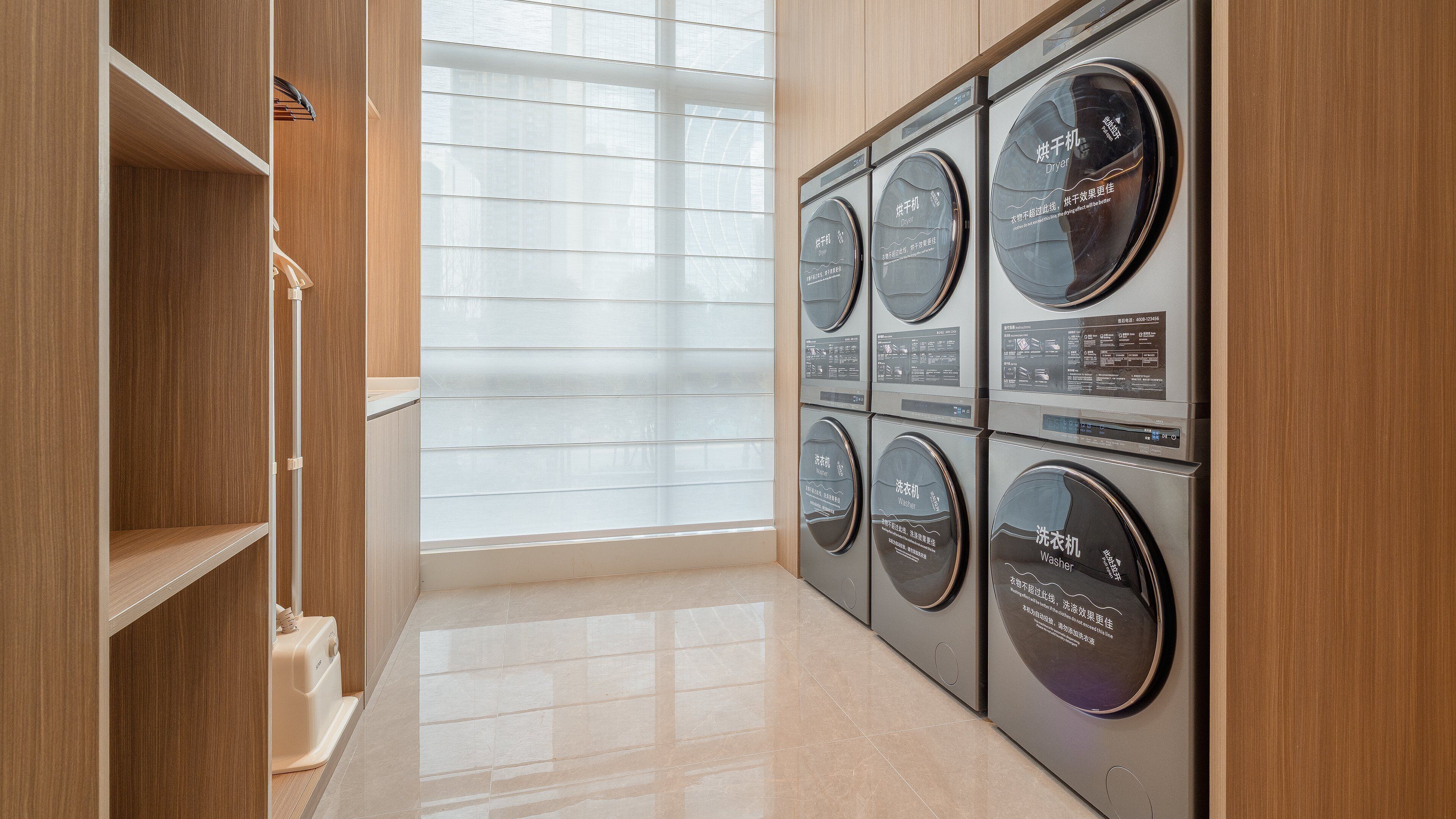 A laundry room with six washing machines and dryers, wooden cabinets, and a large window with blinds.