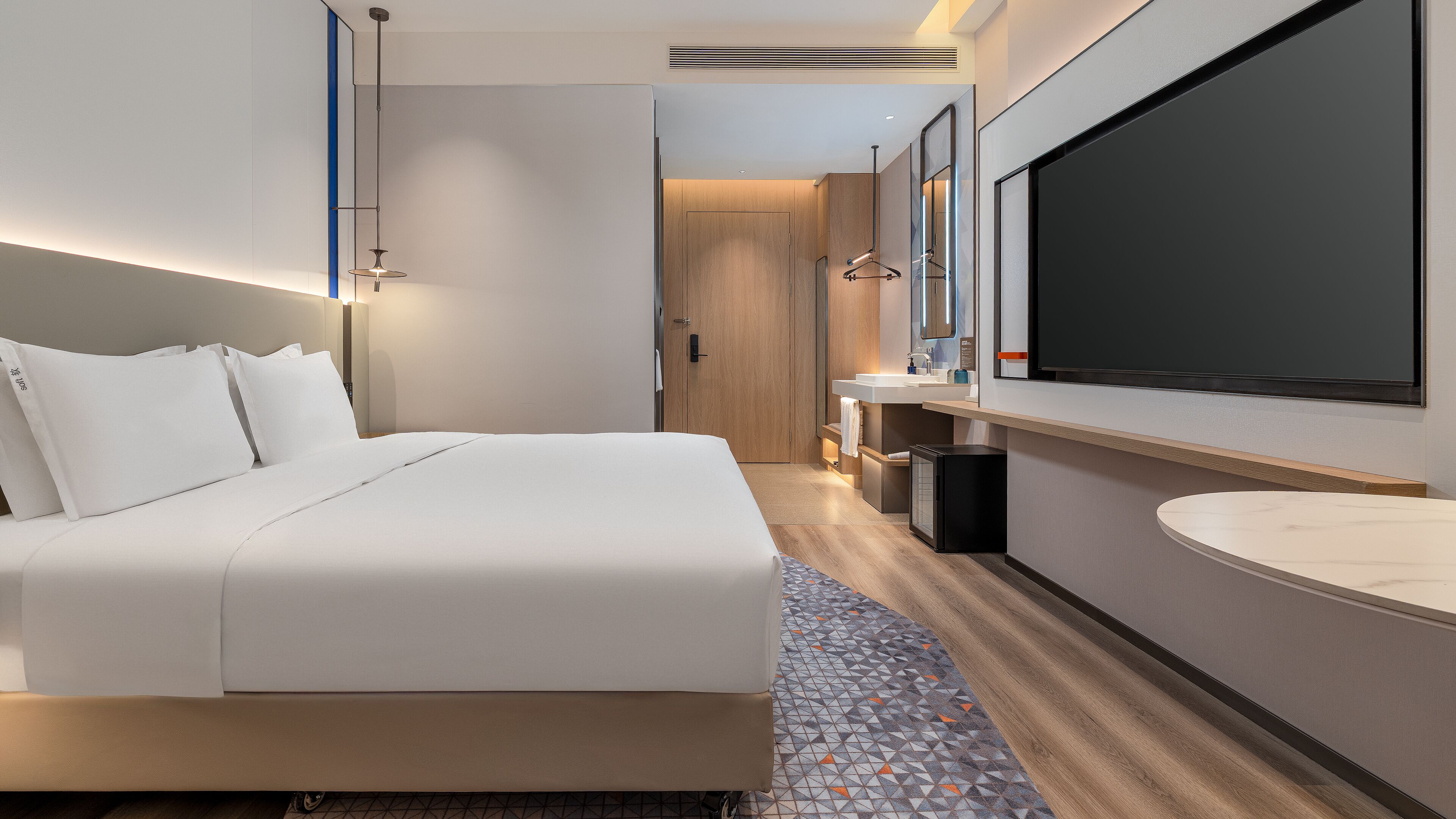 Een moderne hotelkamer met een groot bed, een badkamer met spiegel en wastafel, en een flatscreen televisie.