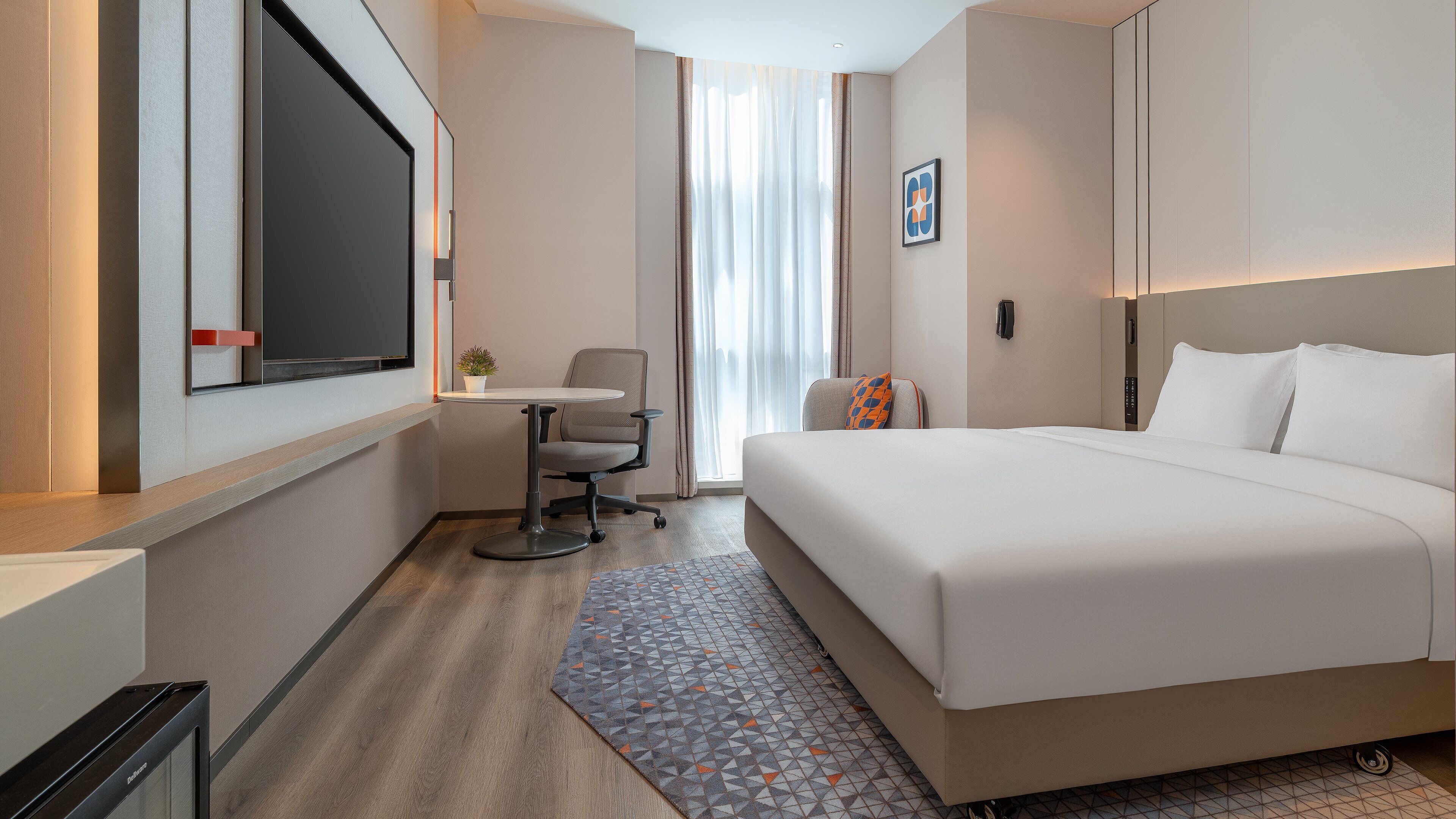 Una habitación de hotel con una cama grande, un escritorio, una silla, una mesita, una planta en maceta y una ventana con cortinas.