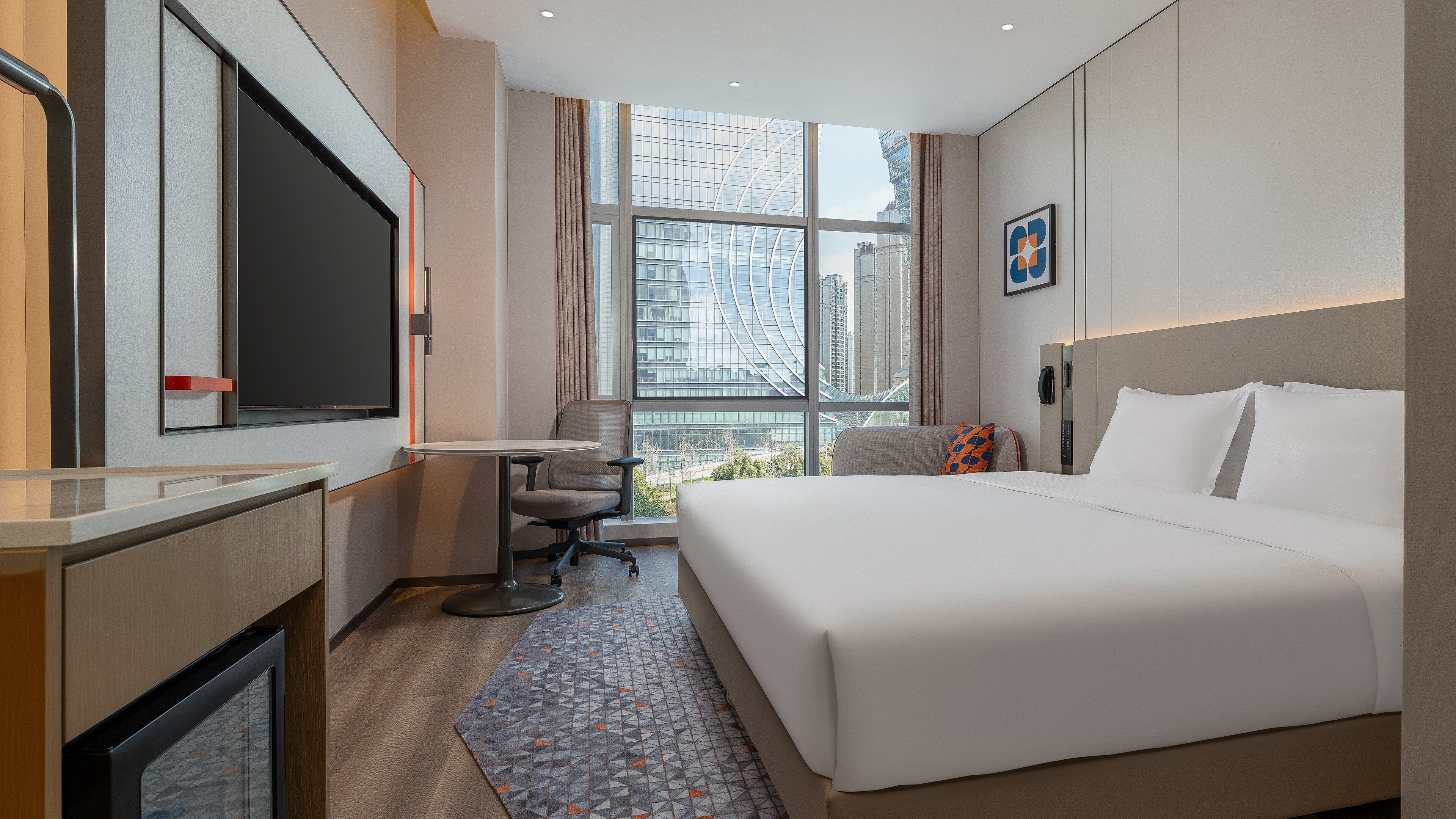 Una camera d'albergo con un letto grande, una scrivania, una sedia, una TV e una finestra con vista sulla città.