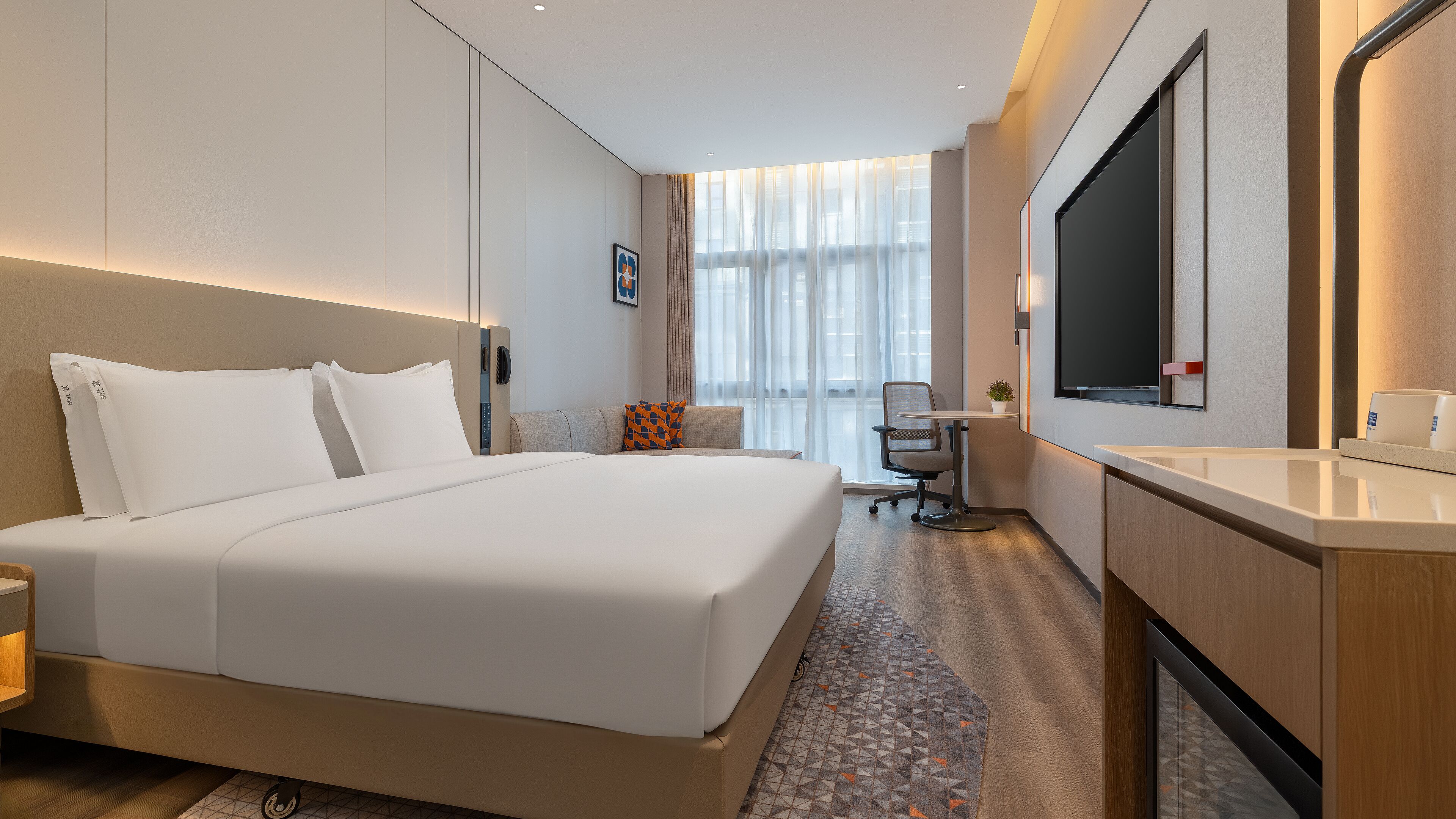 A modern hotel room with a large bed, a desk, a chair, a TV, and a bathroom.