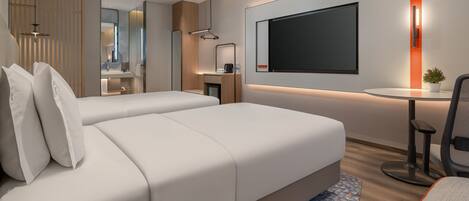 Camera d'albergo moderna con due letti, una scrivania, una TV e una piccola pianta.