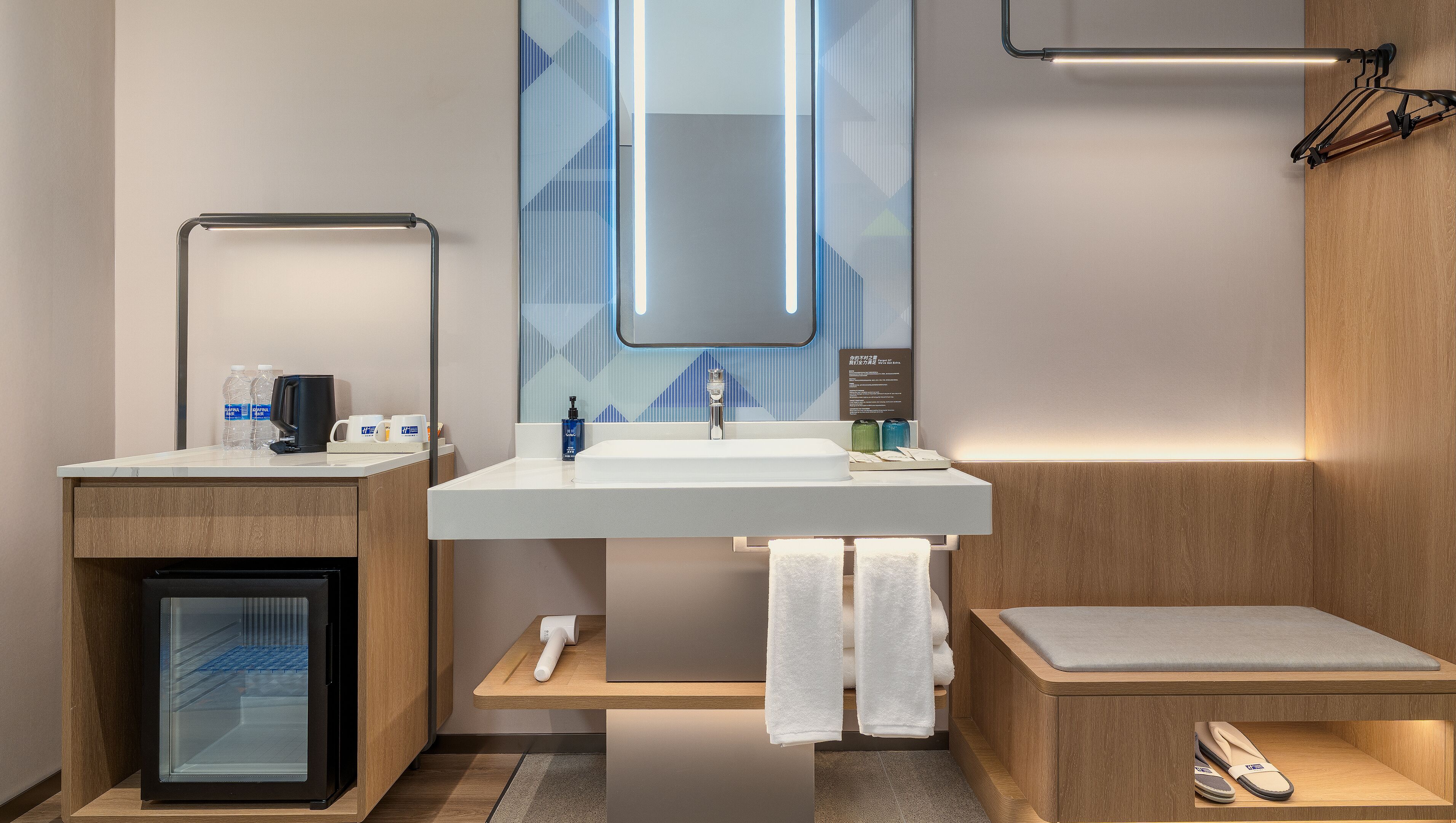 A modern bathroom with a white sink, mirror, and towel rack. There is a small wooden cabinet and a shelf with toiletries.